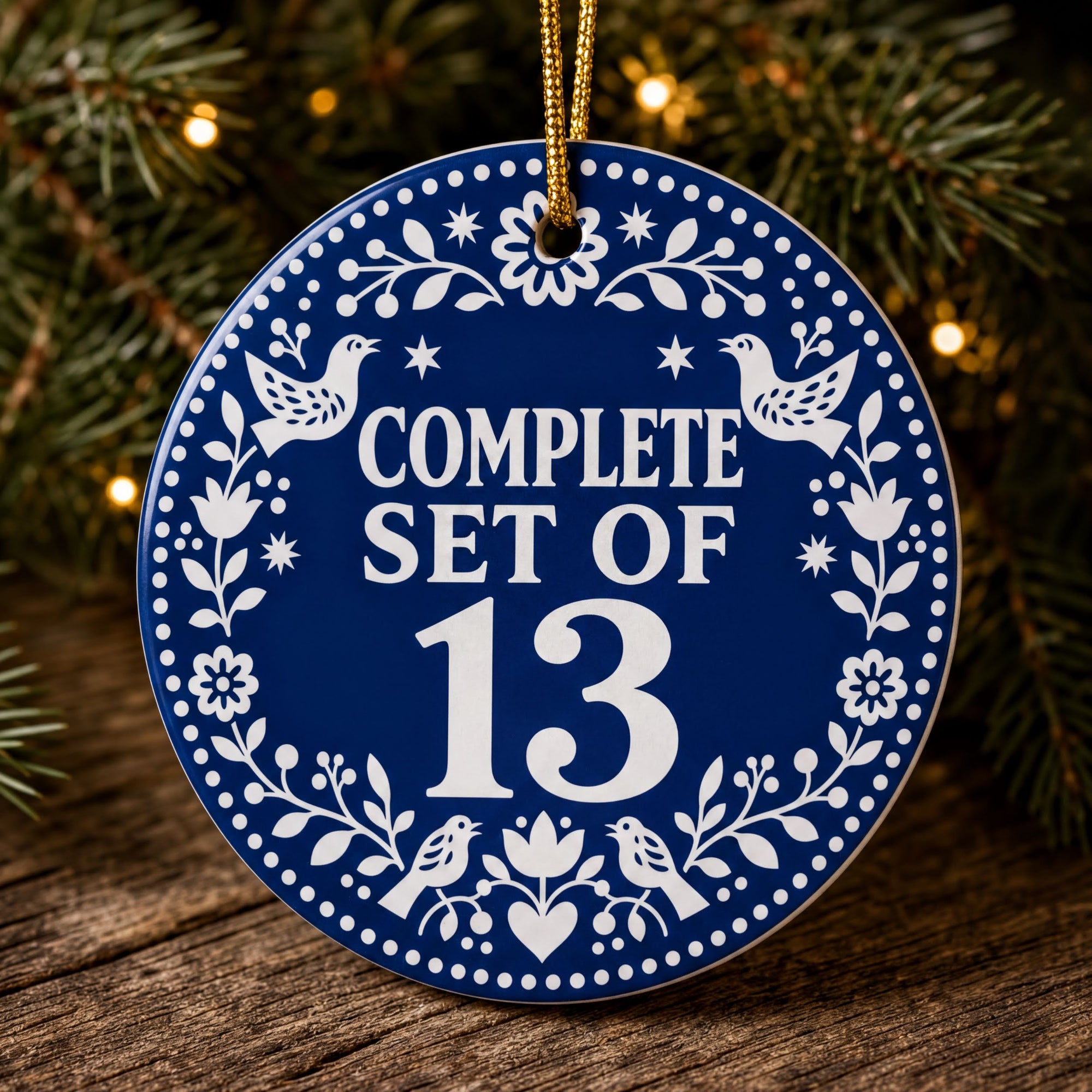 A blue ornament with a gold string, hanging on a Christmas tree. The ornament has a floral design and the text "COMPLETE SET OF 13" is displayed on it.