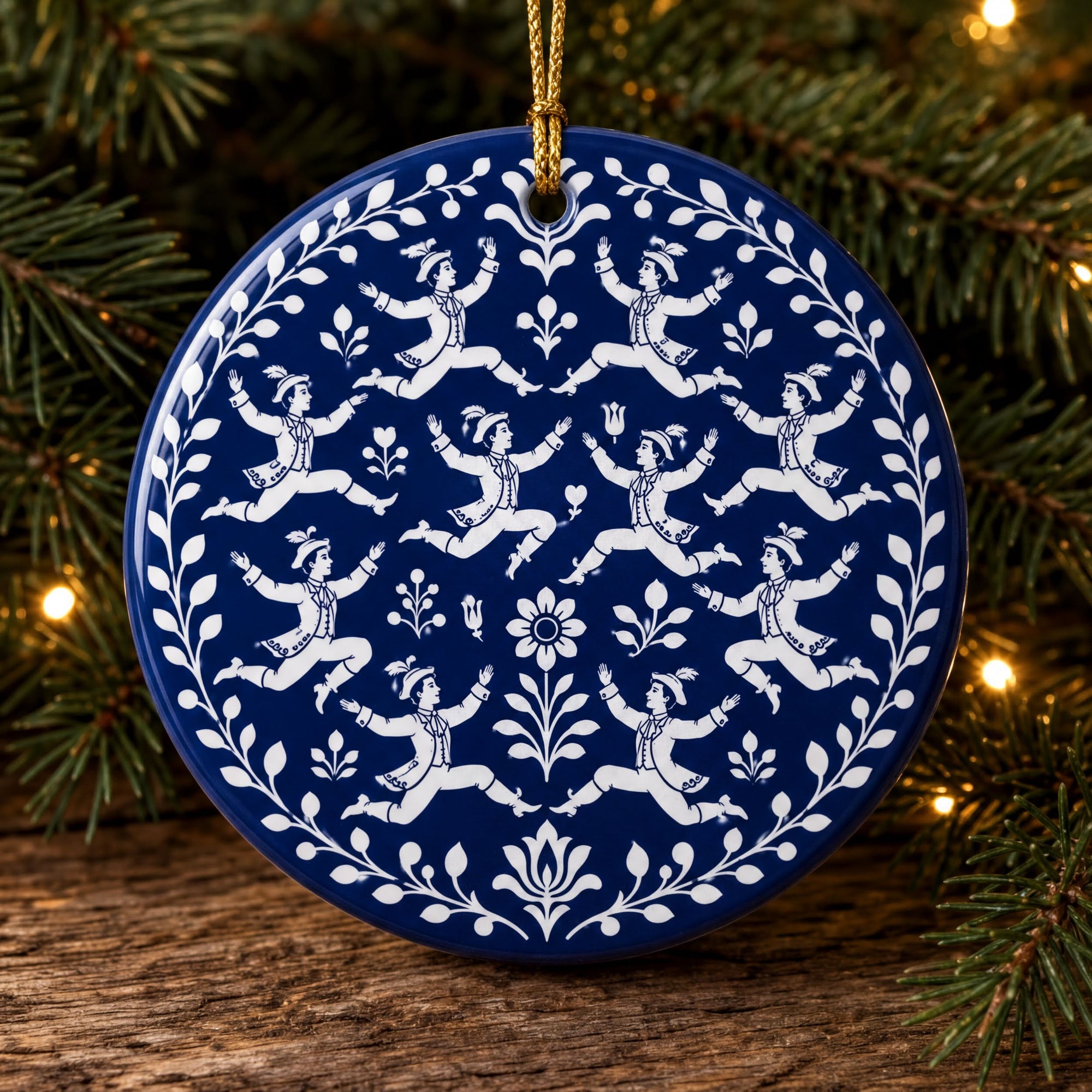 A blue and white ornament with a pattern of dancing figures is hanging on a Christmas tree.